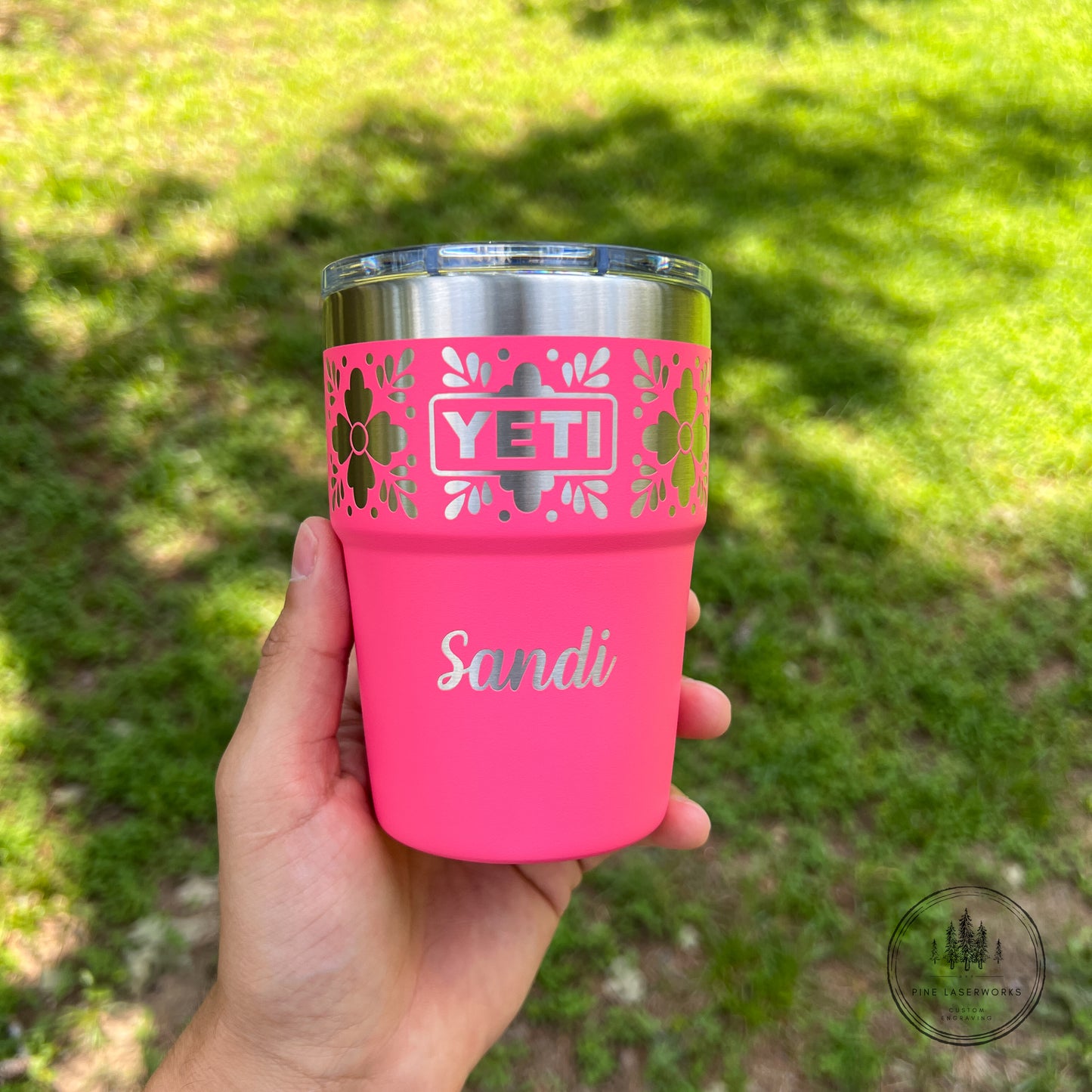 Pink YETI tumbler with 'Sandi' engraved on it, held in a hand against a grassy background.