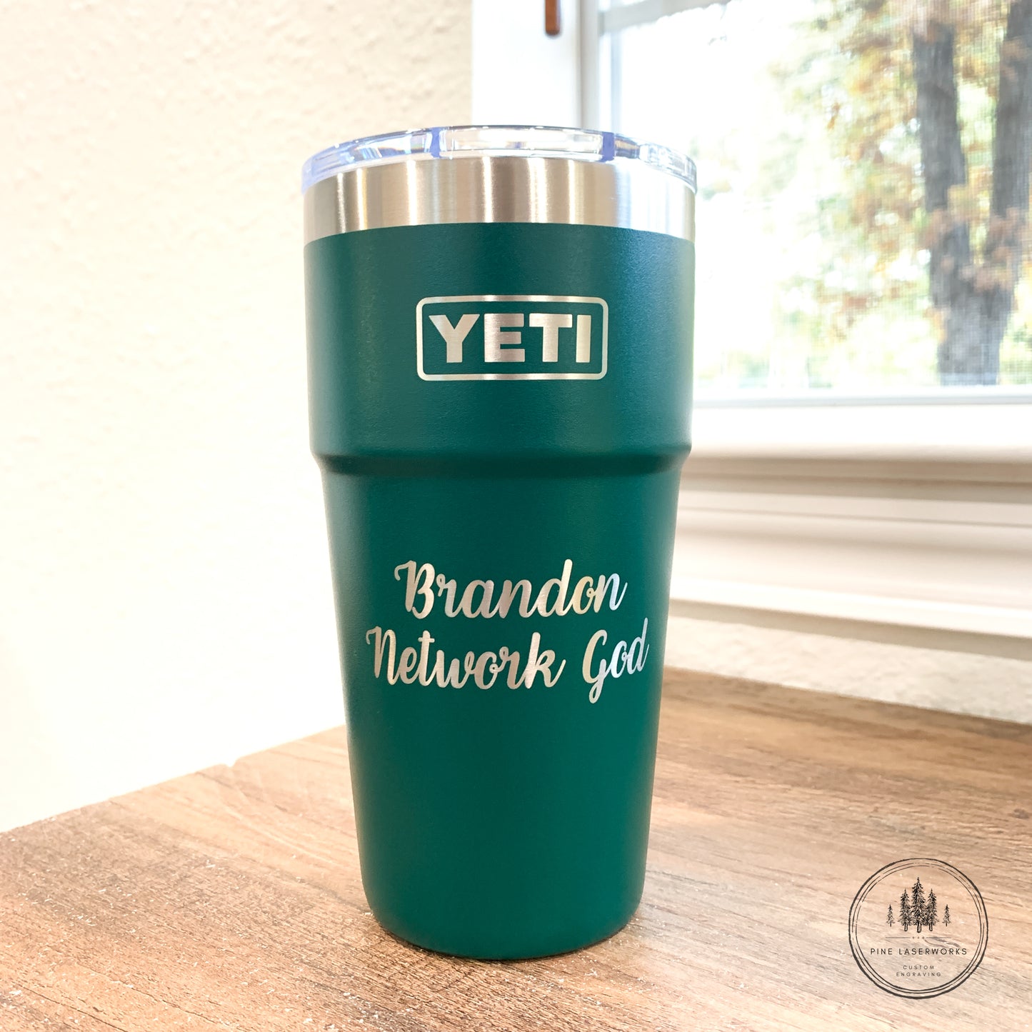 Black Forest Green YETI tumbler with 'Brandon Network God' text on a wooden surface.