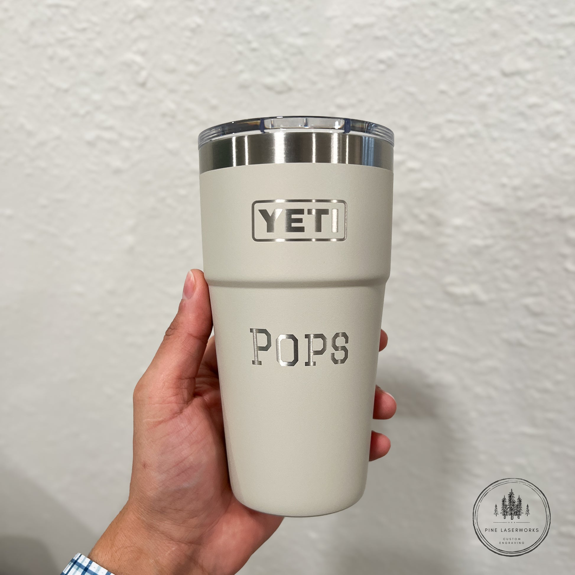 Beige YETI tumbler with 'POPS' engraved, held against a plain background