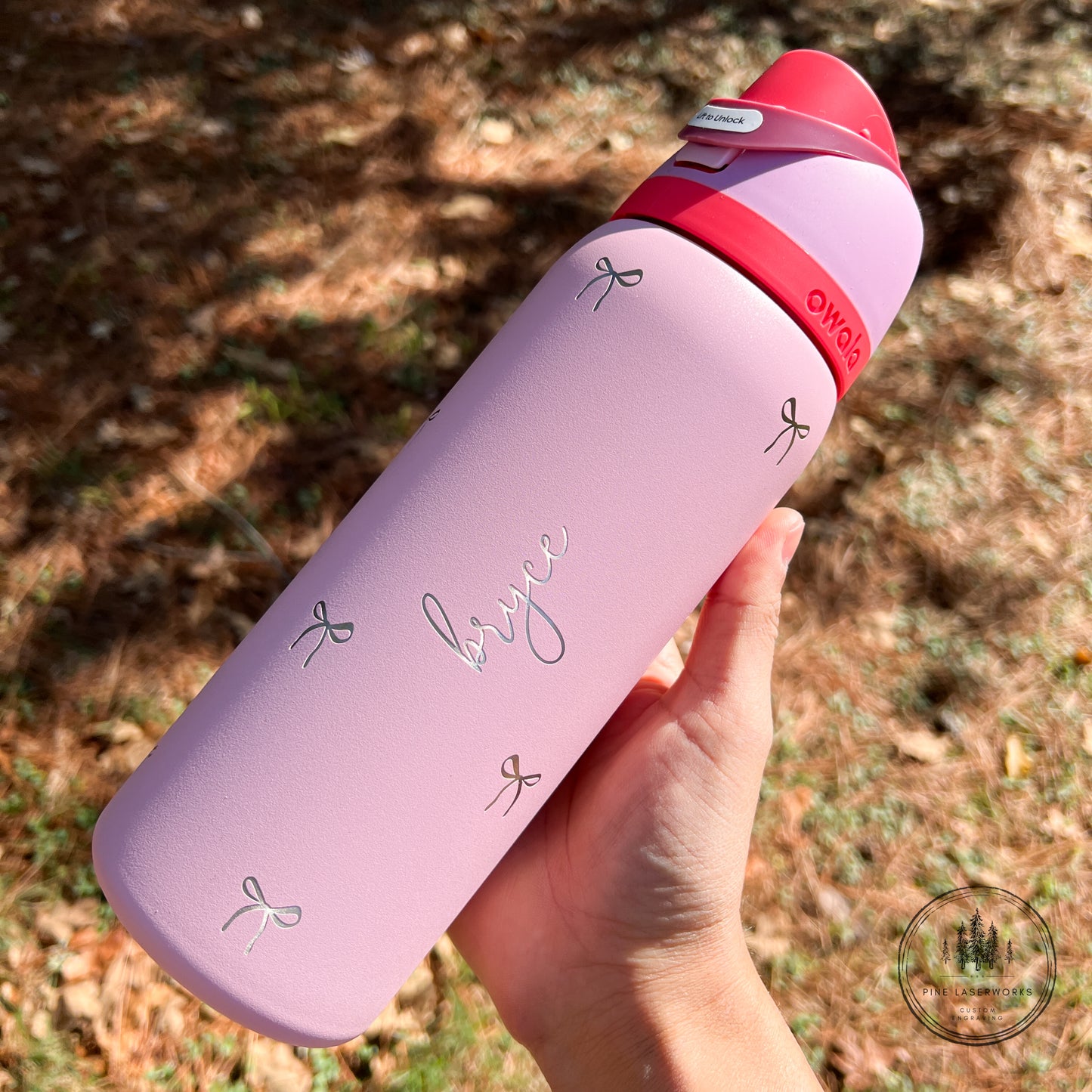 Pink  Owala water bottle with red lid held by a hand outdoors
