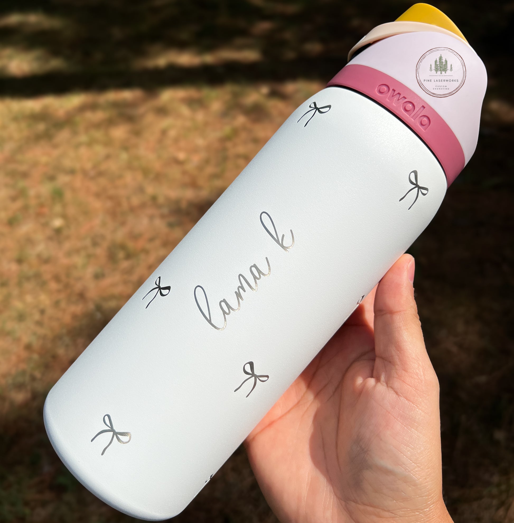 White owala water bottle with 'lama k' branding held by a hand outdoors.