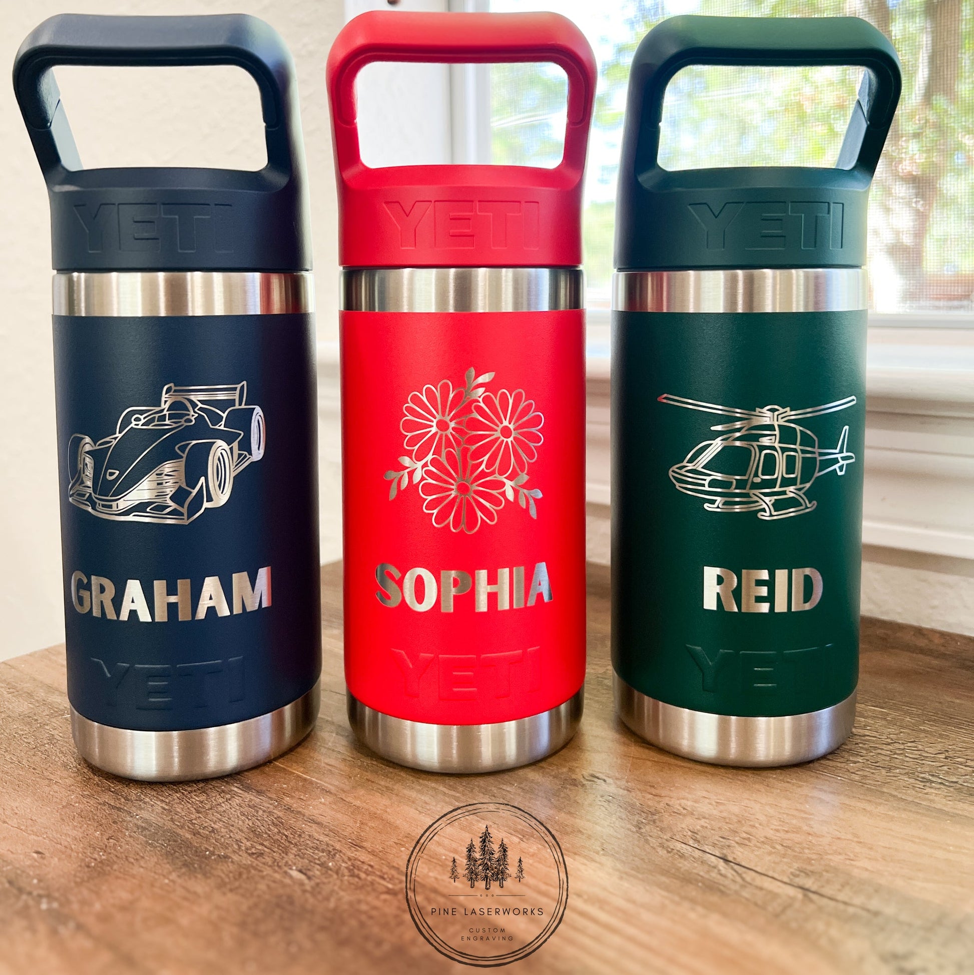 Three insulated YETI drinkware with personalized names on a wooden surface.