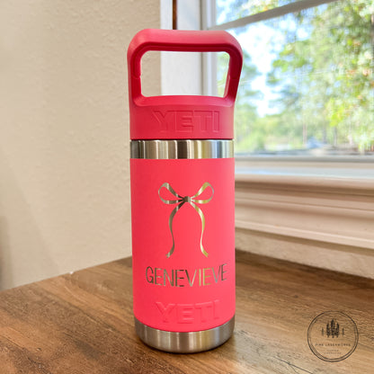 Pink YETI water bottle with 'Genevieve' on a wooden surface near a window.