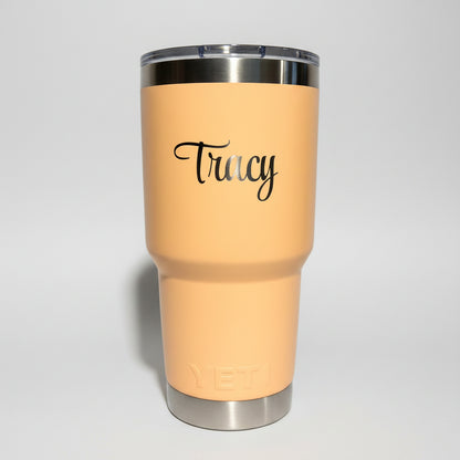 Beige tumbler with 'Fancy' text on a white stand against a gray wall.