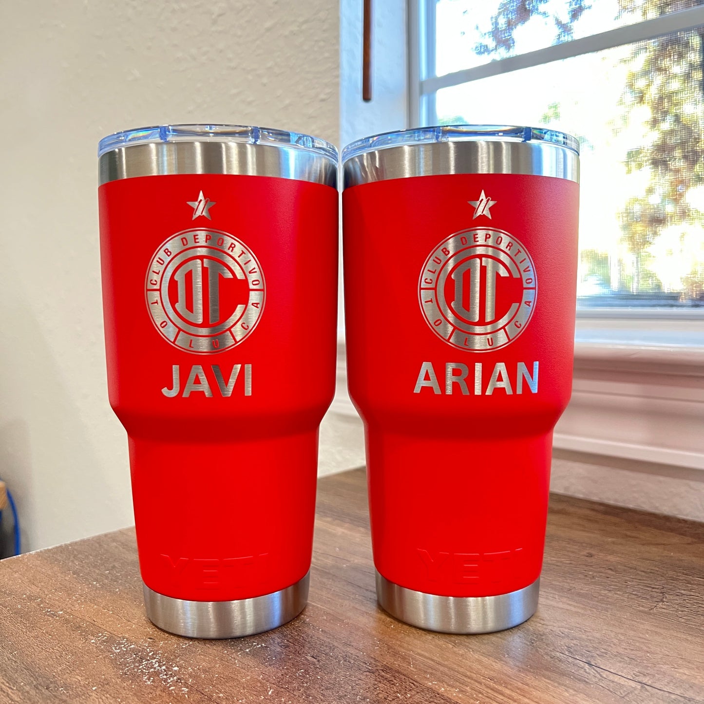 Two red thermos bottles with silver lids on a wooden surface.