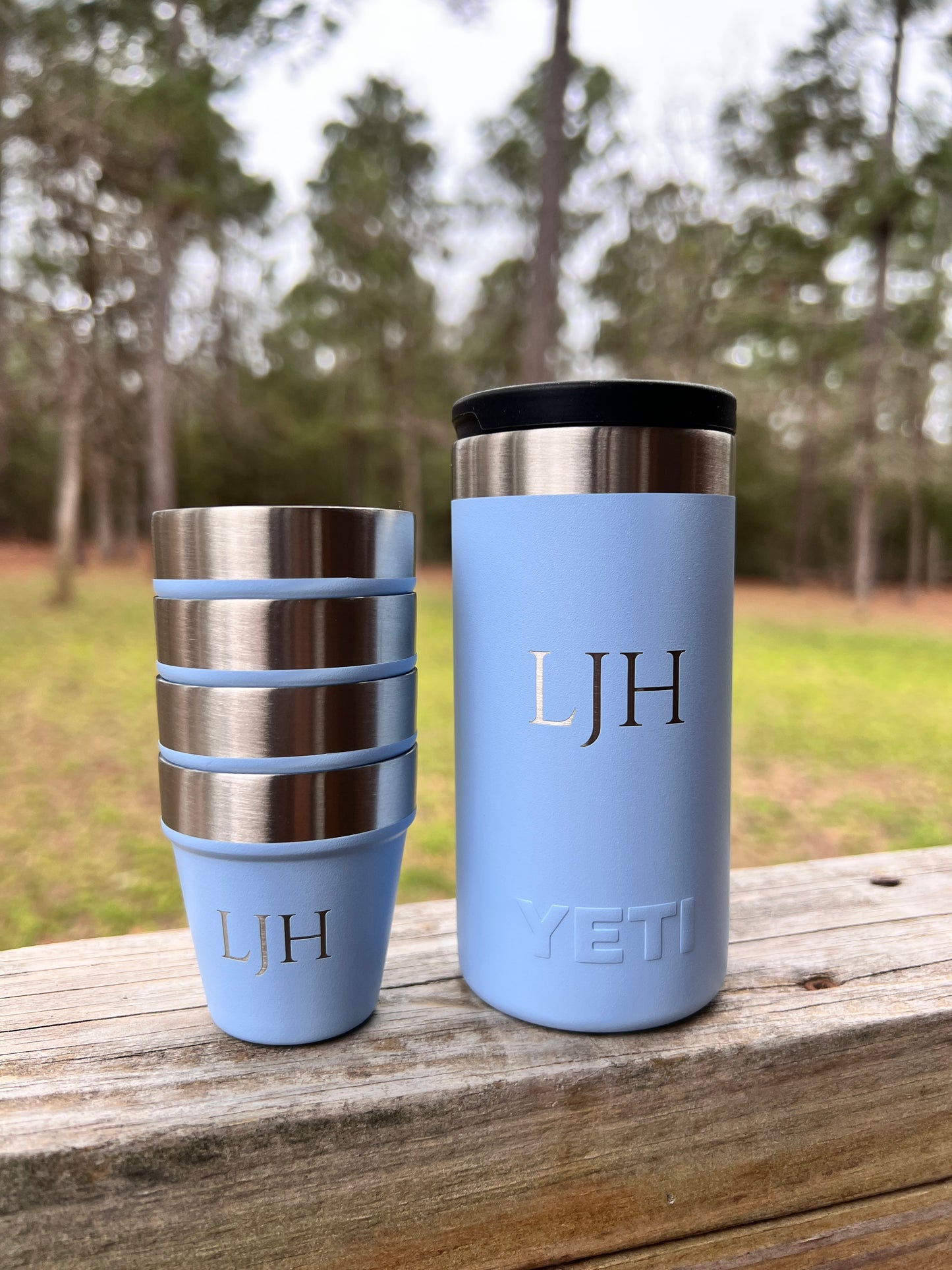 Two light blue YETI tumblers with monogram initials on a wooden surface outdoors.