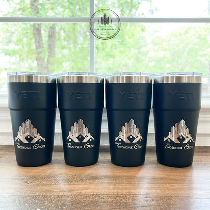 Four black YETI tumblers with a logo on a wooden surface in front of a window.