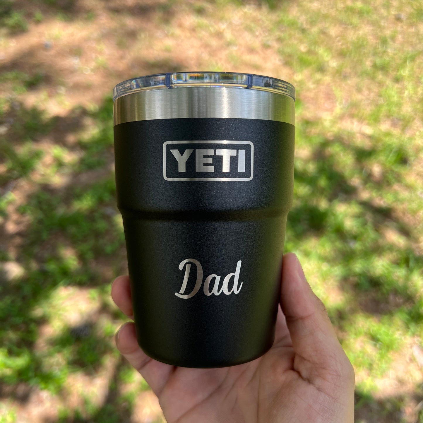 Hand holding a YETI mug with 'Dad' engraved on it against a blurred natural background