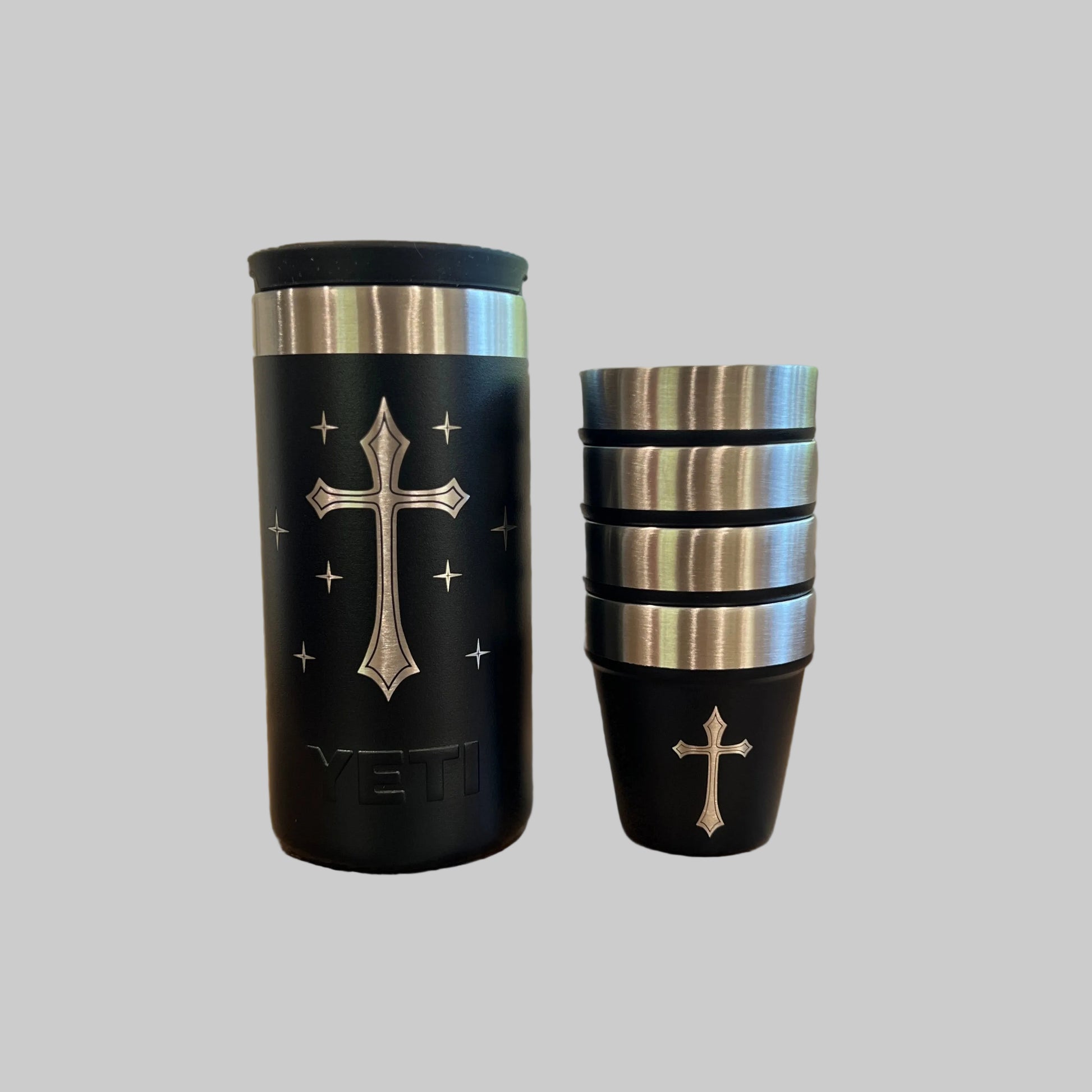Two black travel mugs with silver cross designs on a wooden surface.
