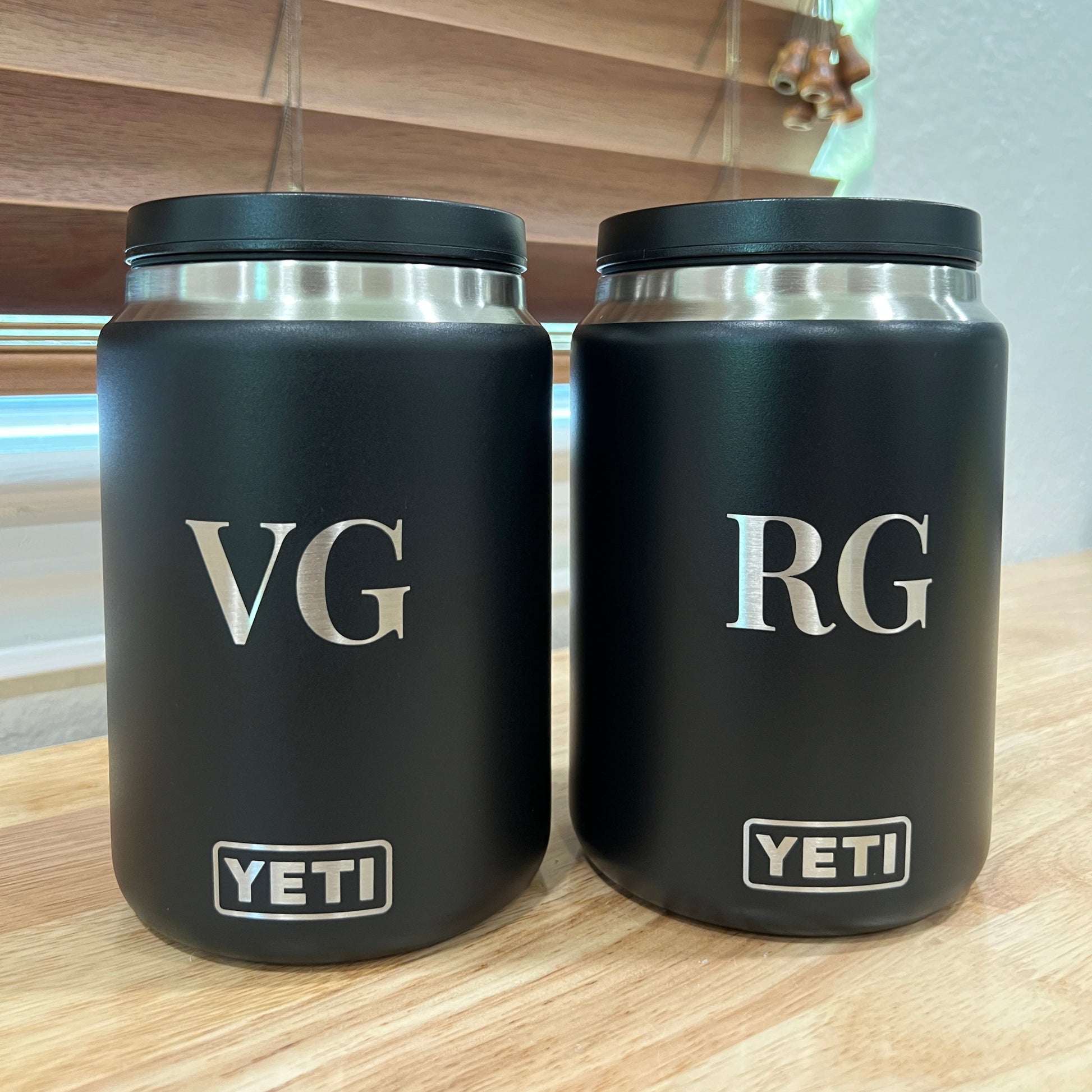 Two black YETI tumblers with initials 'RG' and 'VG' on a reflective surface.