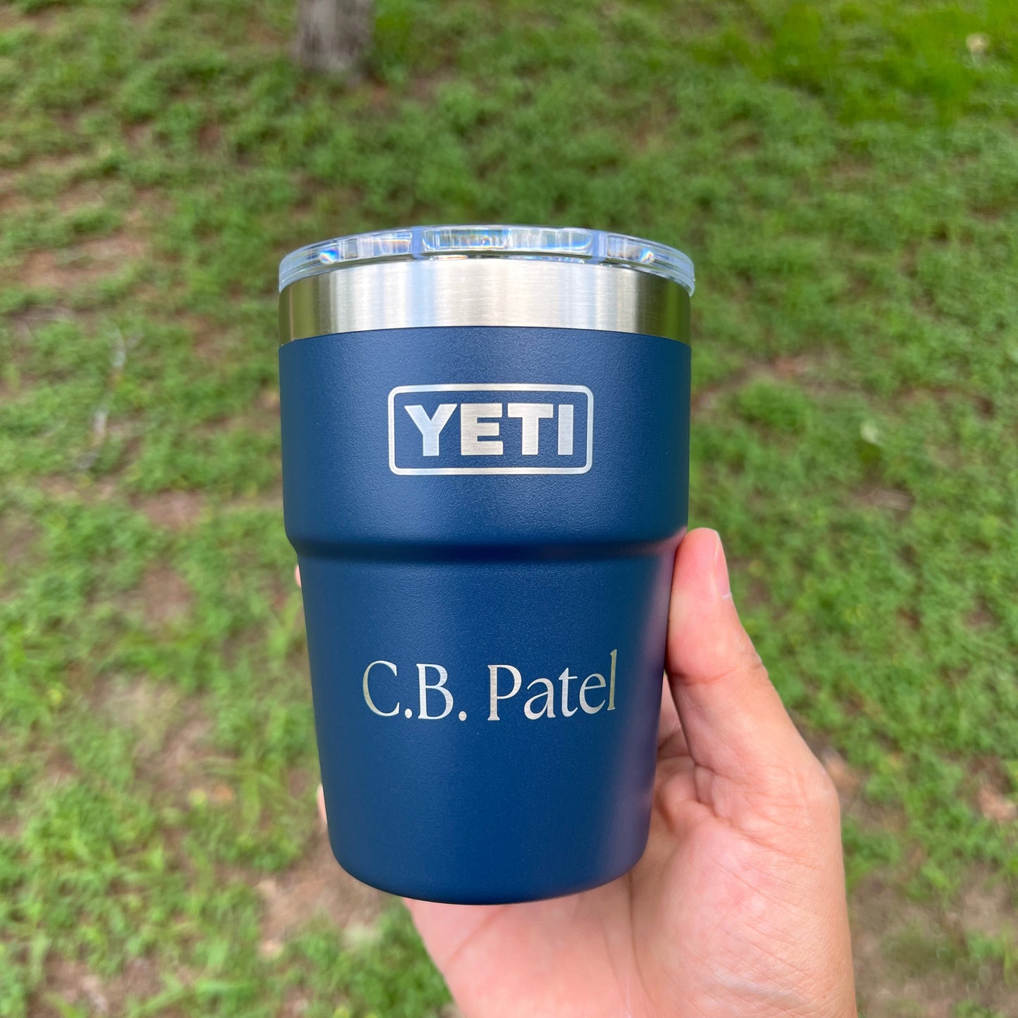 Blue YETI mug with 'C.B. Patel' engraving held by a hand against a grassy background