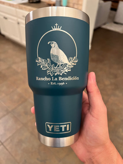 Hand holding a blue YETI mug with a logo and text on a wooden surface