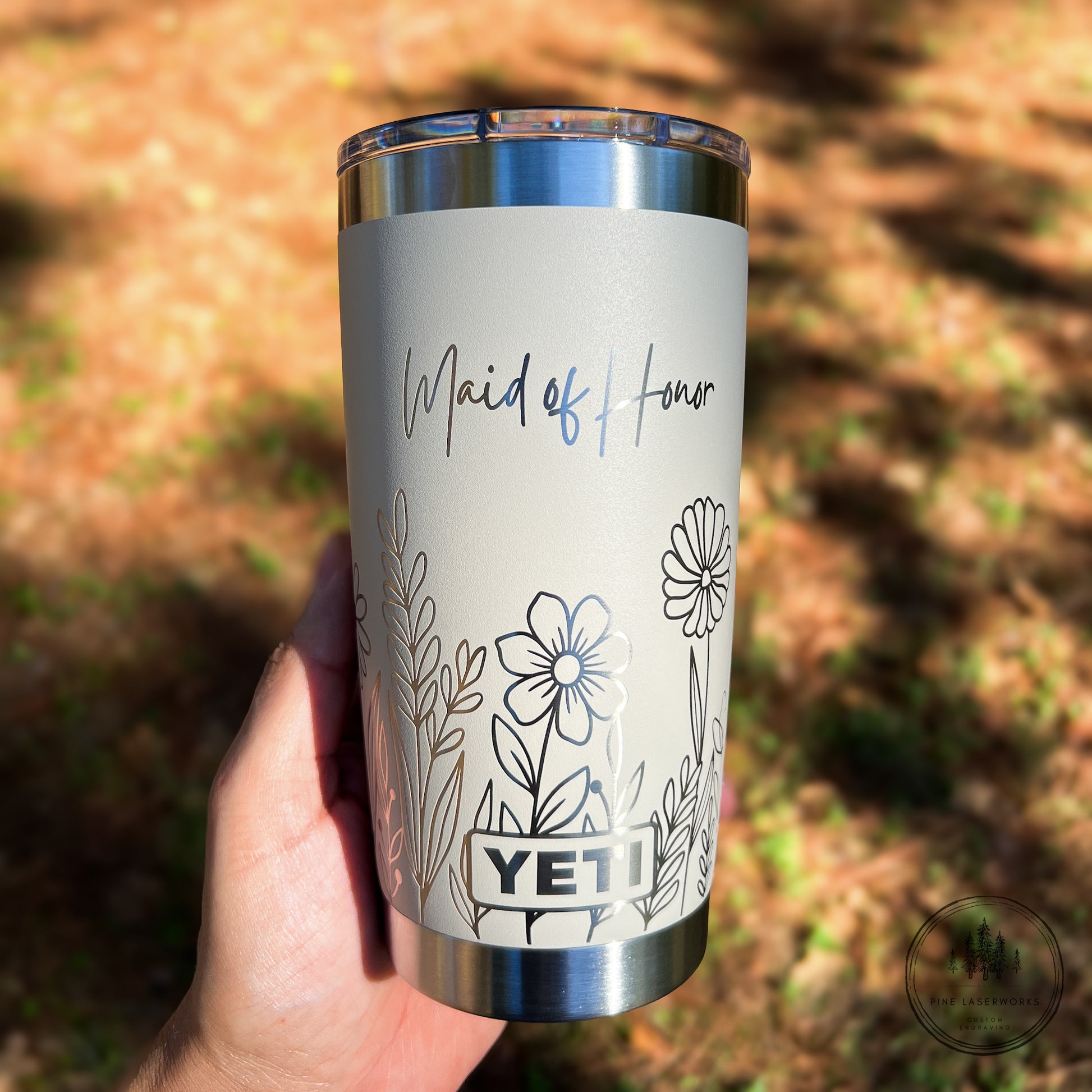 Yeti tumbler with 'Maid of Honor' text and floral design held in a hand outdoors.