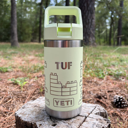 A pale yellow-green YETI TUF water bottle with a stainless steel band and a matching lid, standing on a tree stump in an outdoor forest setting.