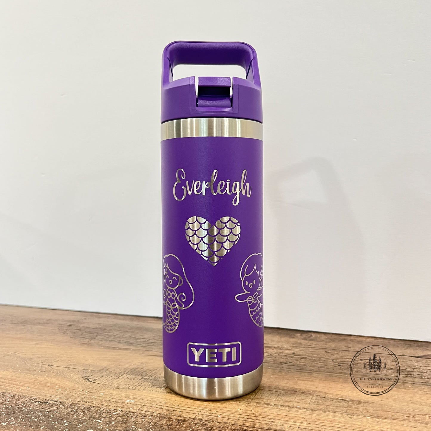 A purple YETI insulated travel tumbler with a matching purple lid and handle, featuring the name 'Everleigh' and a heart design on the front, standing on a wooden surface against a plain wall.