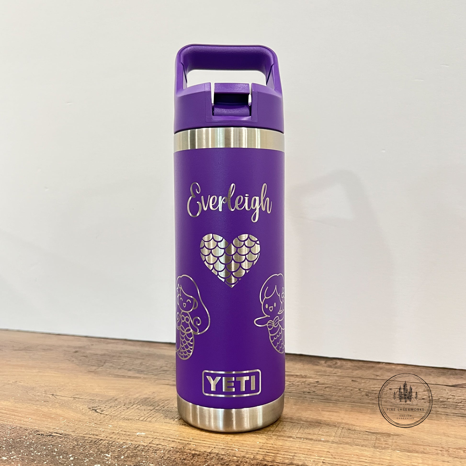 A purple YETI insulated travel tumbler with a matching purple lid and handle, featuring the name 'Everleigh' and a heart design on the front, standing on a wooden surface against a plain wall.