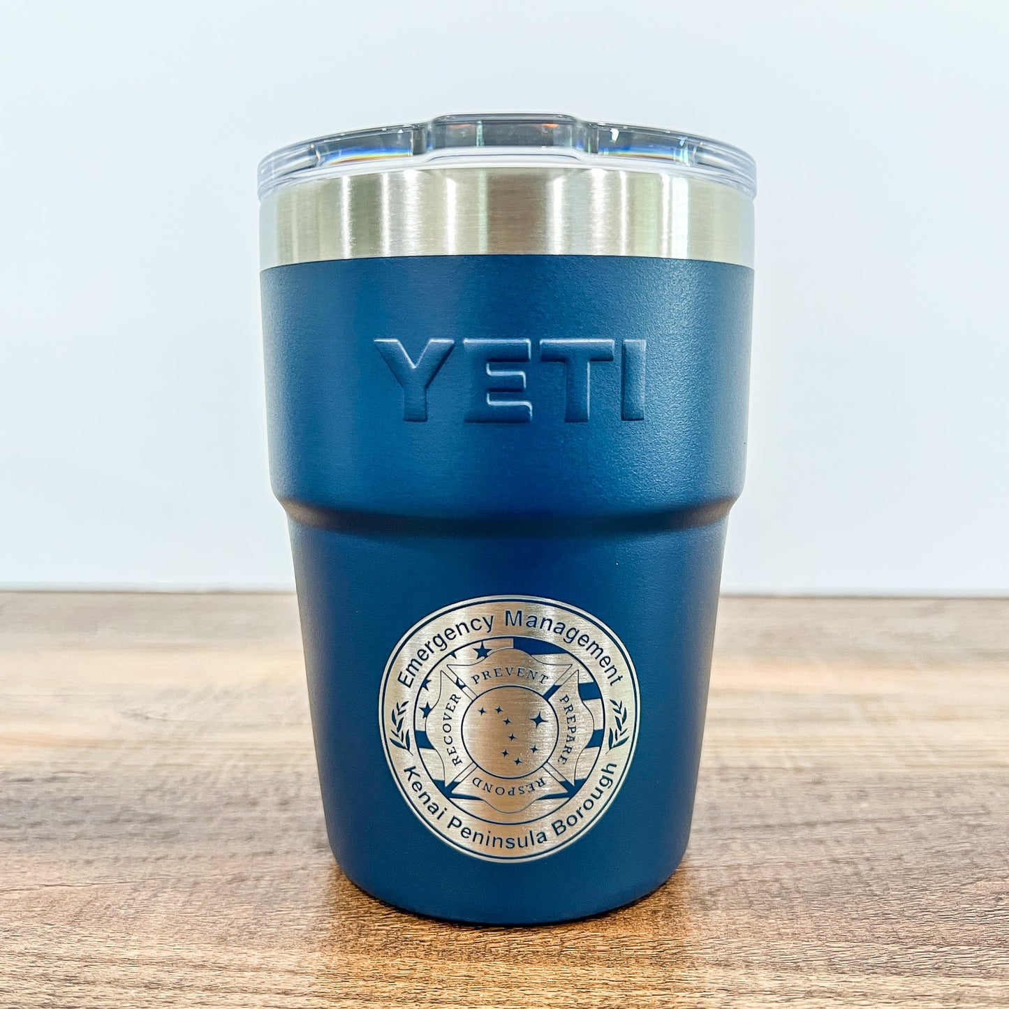 Navy Colored Yeti 16oz Rambler Stackable Tumbler with a round laser engraved logo on a wooden surface. 