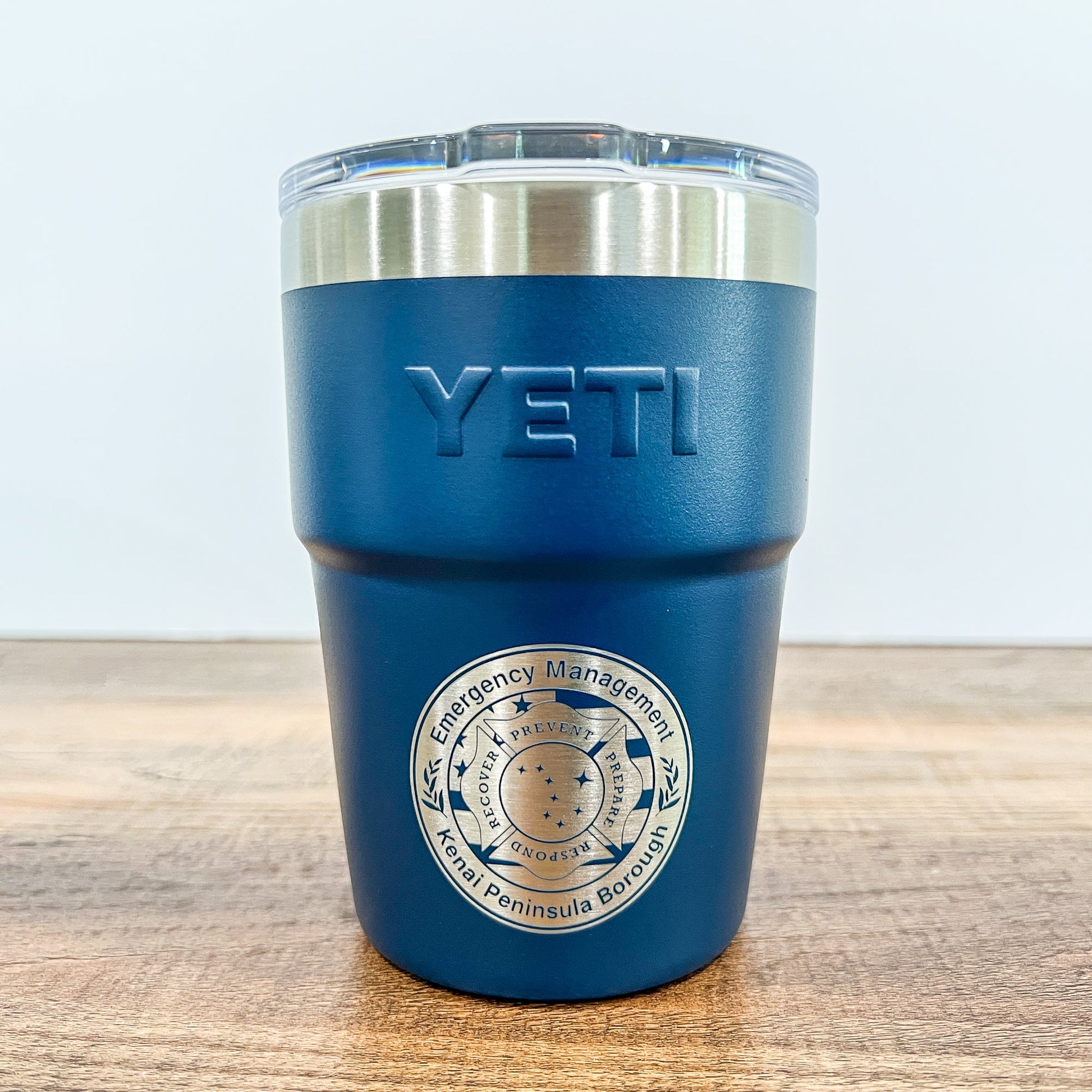 Navy Colored Yeti 16oz Rambler Stackable Tumbler with a round laser engraved logo on a wooden surface. 