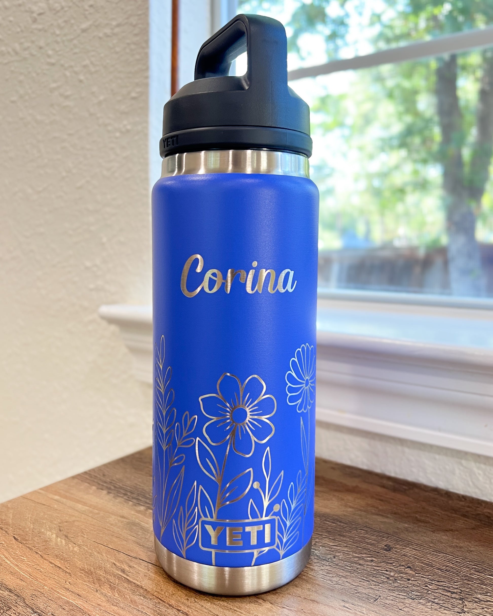 Personalized Floral Yeti 26oz or 36oz Rambler Laser Engraved Water Bottle - Pine LaserworksUltraviolet Marine YETI water bottle with floral design and 'Corina' engraving on a wooden surface.