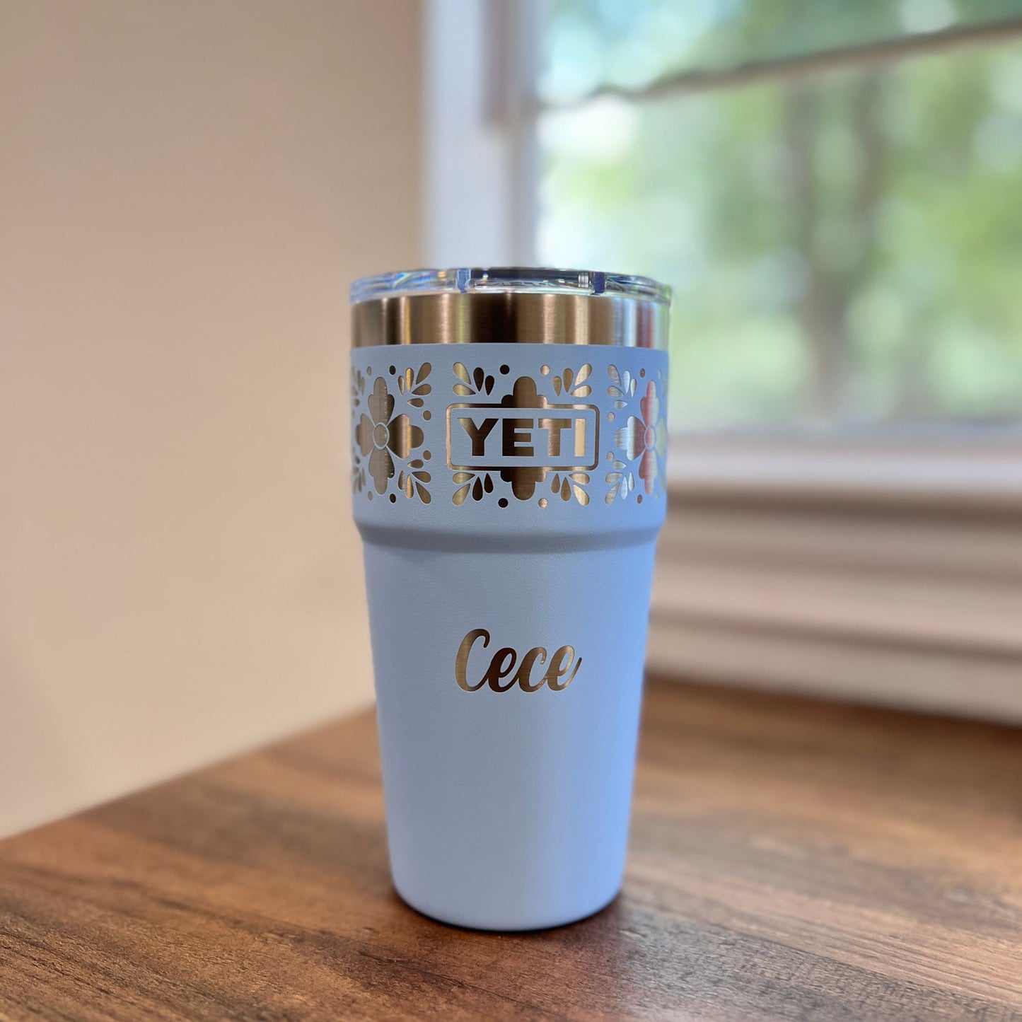 Personalized Talavera Flower Yeti 20oz Stackable Cup - Pine LaserworksBig Sky Blue YETI tumbler with decorative side on a wooden surface near a window.