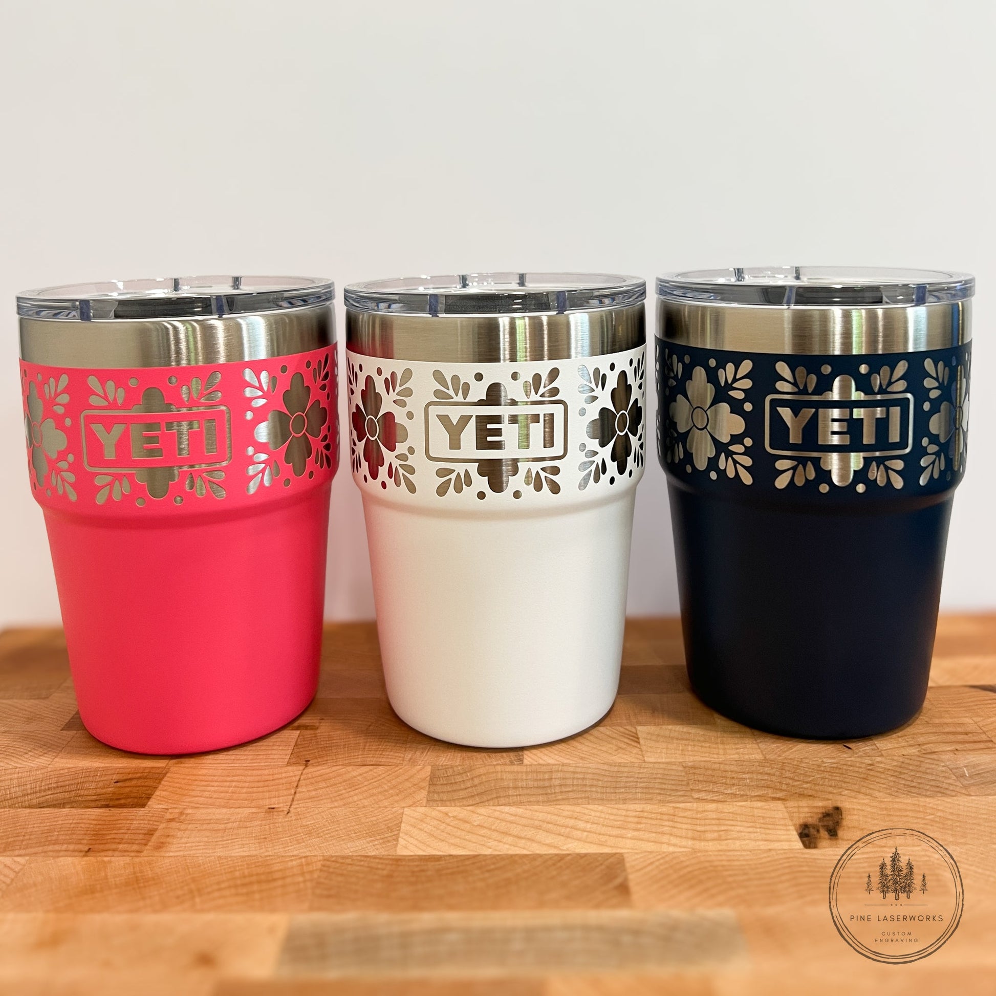 Talavera Flower Yeti 16oz Stackable Cup - Pine LaserworksThree YETI tumblers in pink, white, and navy on a wooden surface with a light background.